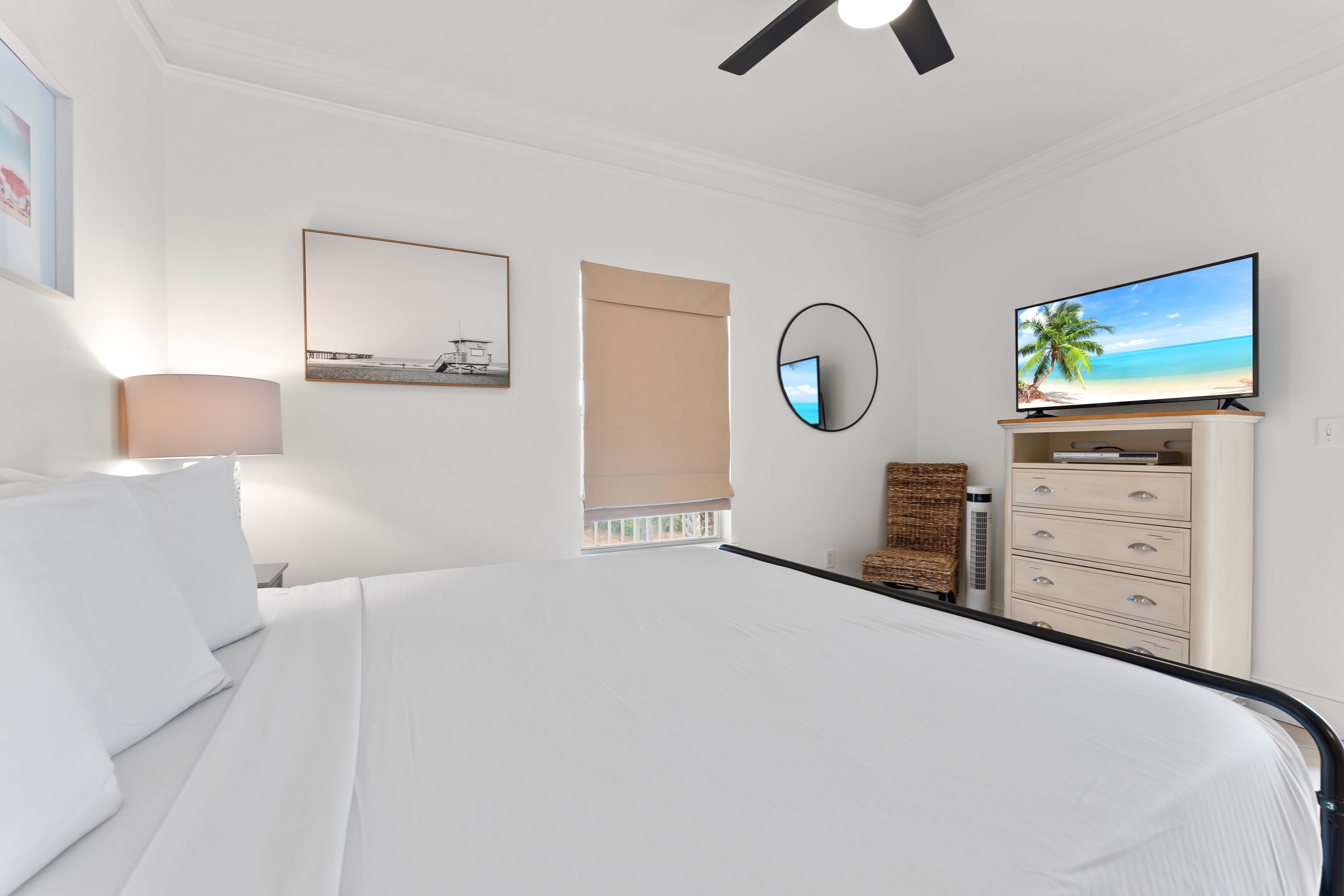 A hotel room with a bed, a television, a dresser, and a window with a view of a beach.