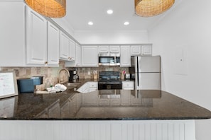Une cuisine moderne avec des meubles blancs, un plan de travail en granit, des appareils électroménagers en acier inoxydable et un luminaire suspendu au plafond en osier.