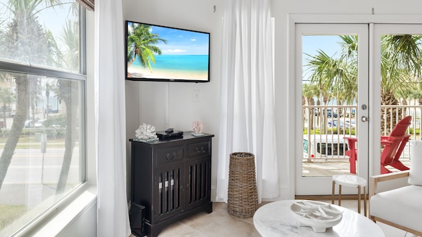 A room with a TV displaying a beach scene, a dark wooden cabinet, a wicker basket, and a white chair. - Crystal Beach. Caribbean Dunes. Completely Renovated. Corner Unit. Gulf View.  (Destin)