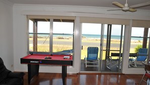 Ein Zimmer mit Billardtisch, Deckenventilator und Blick auf den Strand durch große Schiebetüren.