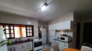 Kompakti keittiö, jossa on valkoiset kaapit, mikroaaltouuni ja jääkaappi. Ikkunasta avautuu näkymä vehreään maisemaan.
