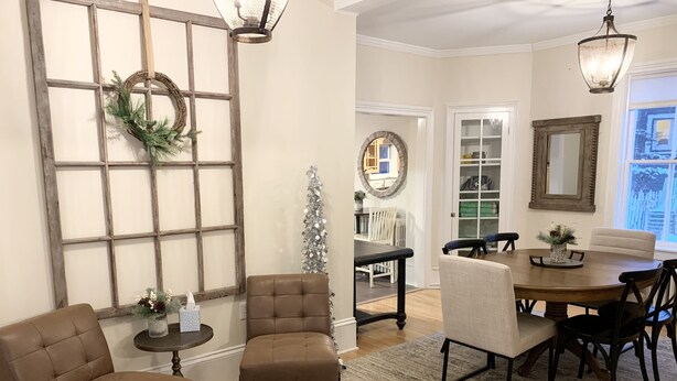 A dining area with a round table, chairs, and a glass-top coffee table. There is a large window with a wooden frame and a wreath on it. - Spacious home w/Hot Tub near Lake Superior walk to restaurants, breweries, beach (Marquette)
