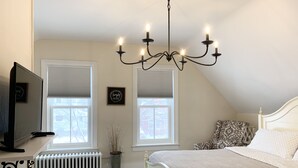 A bedroom with a bed, a chandelier, a radiator, and two windows with blinds. - Spacious home w/Hot Tub near Lake Superior walk to restaurants, breweries, beach (Marquette)