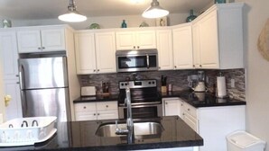 A modern kitchen with white cabinets, stainless steel appliances, a black countertop, and pendant lighting.
