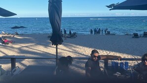 A beachside restaurant with outdoor seating, umbrellas, and a view of the ocean.