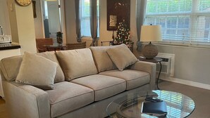 A living room with a beige sofa, a glass coffee table, and a dining area with a wicker table and chairs.