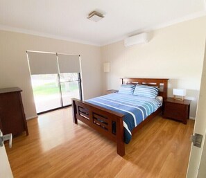 Un dormitorio con cama de madera, mesita de noche, lámpara y puerta corrediza de vidrio que da a un balcón.