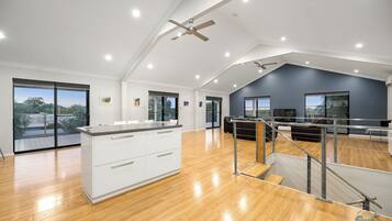 A spacious living area with a high ceiling, a kitchen with white cabinets, and a balcony with a view.