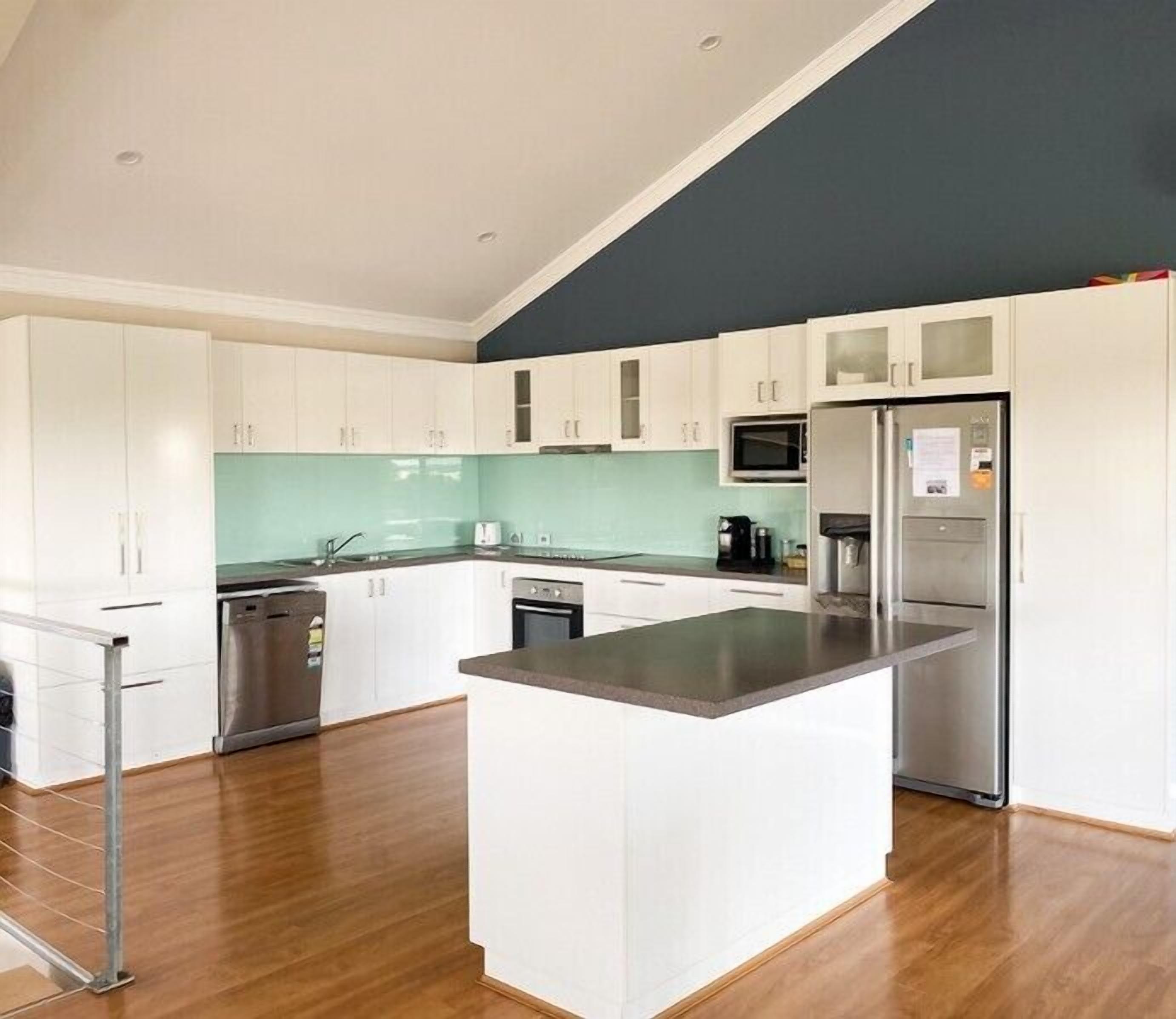 A modern kitchen with white cabinets, a central island, stainless steel appliances, and a teal backsplash.
