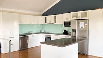 A modern kitchen with white cabinets, a central island, stainless steel appliances, and a teal backsplash.