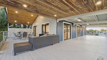 A covered outdoor deck with a dining area, seating, and a view of the surrounding landscape.