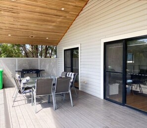 Un patio al aire libre con una mesa, sillas, techo de madera y un ventanal corredero.