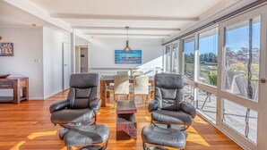 Une pièce spacieuse avec une grande fenêtre, un coin repas comprenant une table et des chaises, et deux fauteuils en cuir au premier plan.