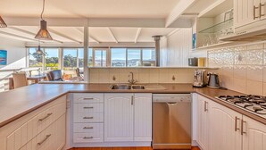Une cuisine moderne avec des meubles blancs, un lave-vaisselle encastré, une cuisinière à gaz et une grande fenêtre donnant sur l’extérieur.