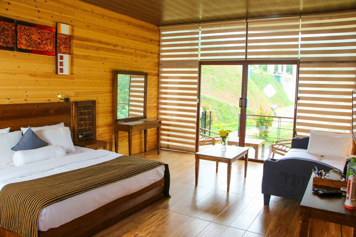 A hotel room with a large bed, a desk, a chair, and a balcony with a view.