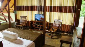 A room with a bed, two wooden chairs, a small table, a television, and curtains.