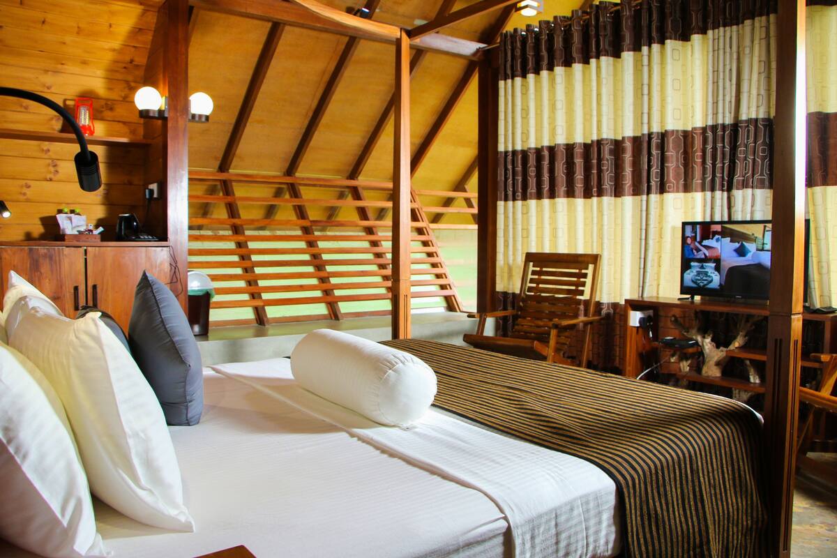 A wooden room with a bed, pillows, a television, and a desk with a lamp.