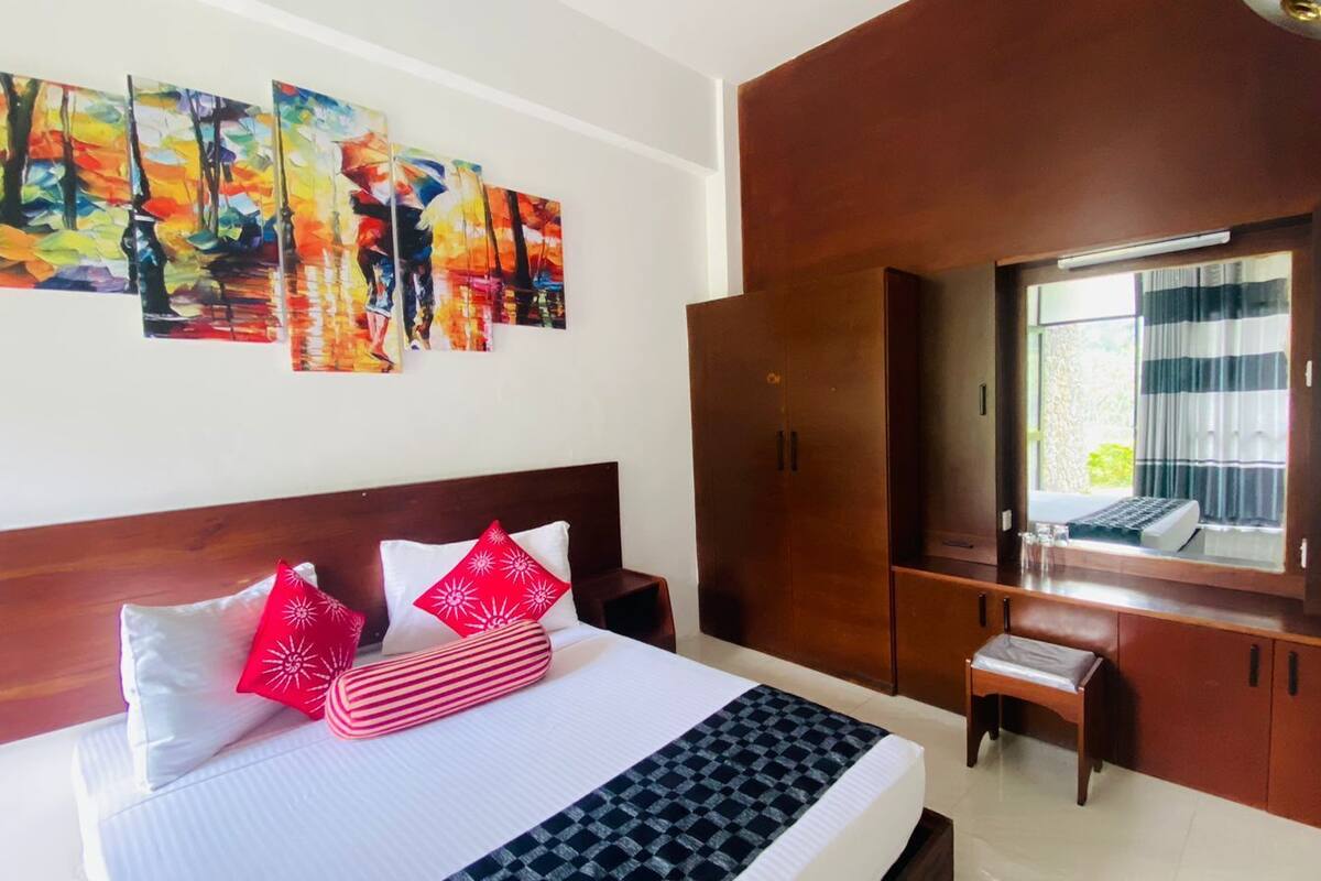 A hotel room with a bed, a desk with a computer, a wardrobe, and a large window.