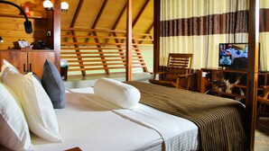A wooden room with a bed, pillows, a desk with a lamp, a chair, and a television. - Aloft Grand Hotel (Kumbalwela)