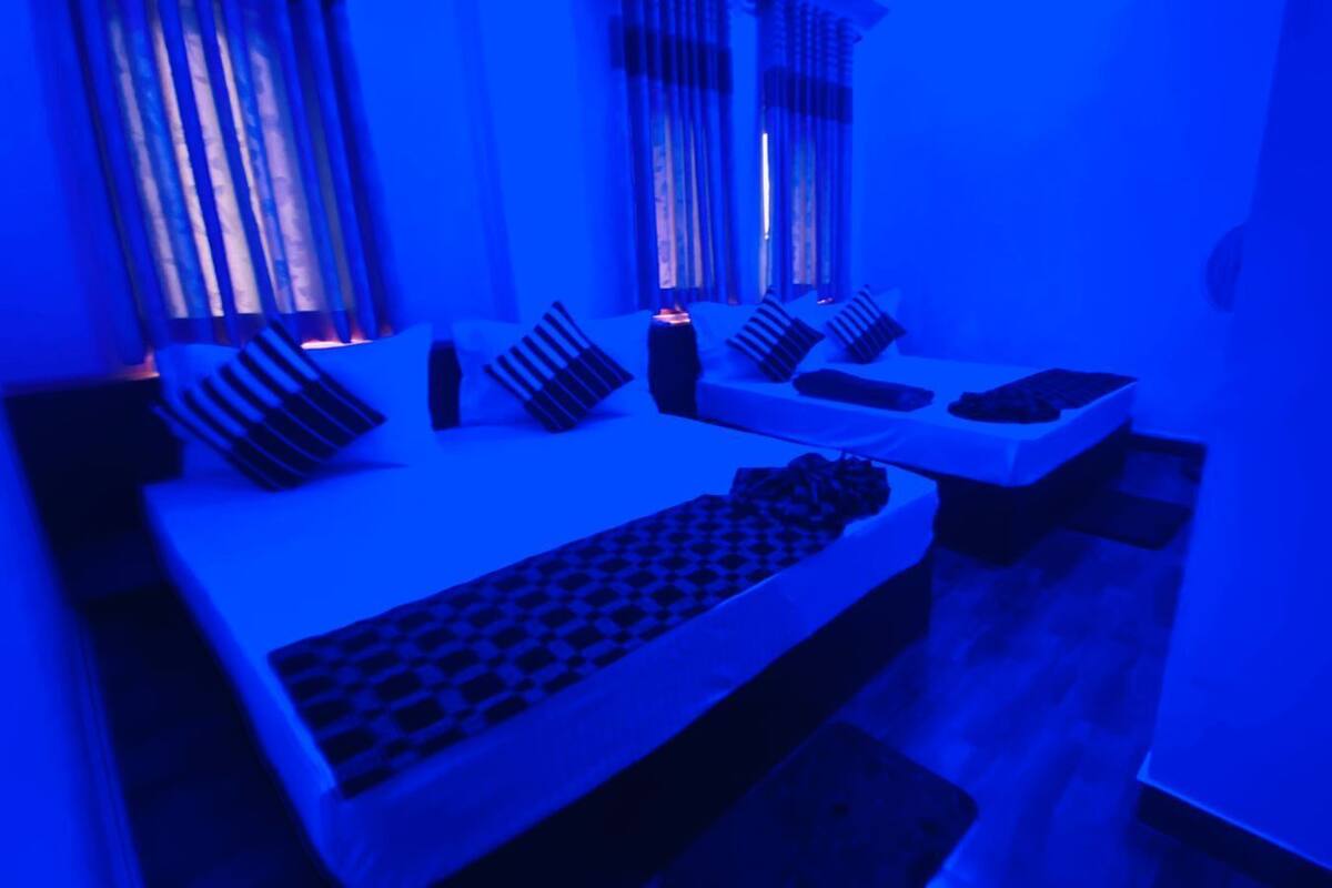 A room with a bed, a desk, and a chair. There are pillows on the bed and a lamp on the desk.