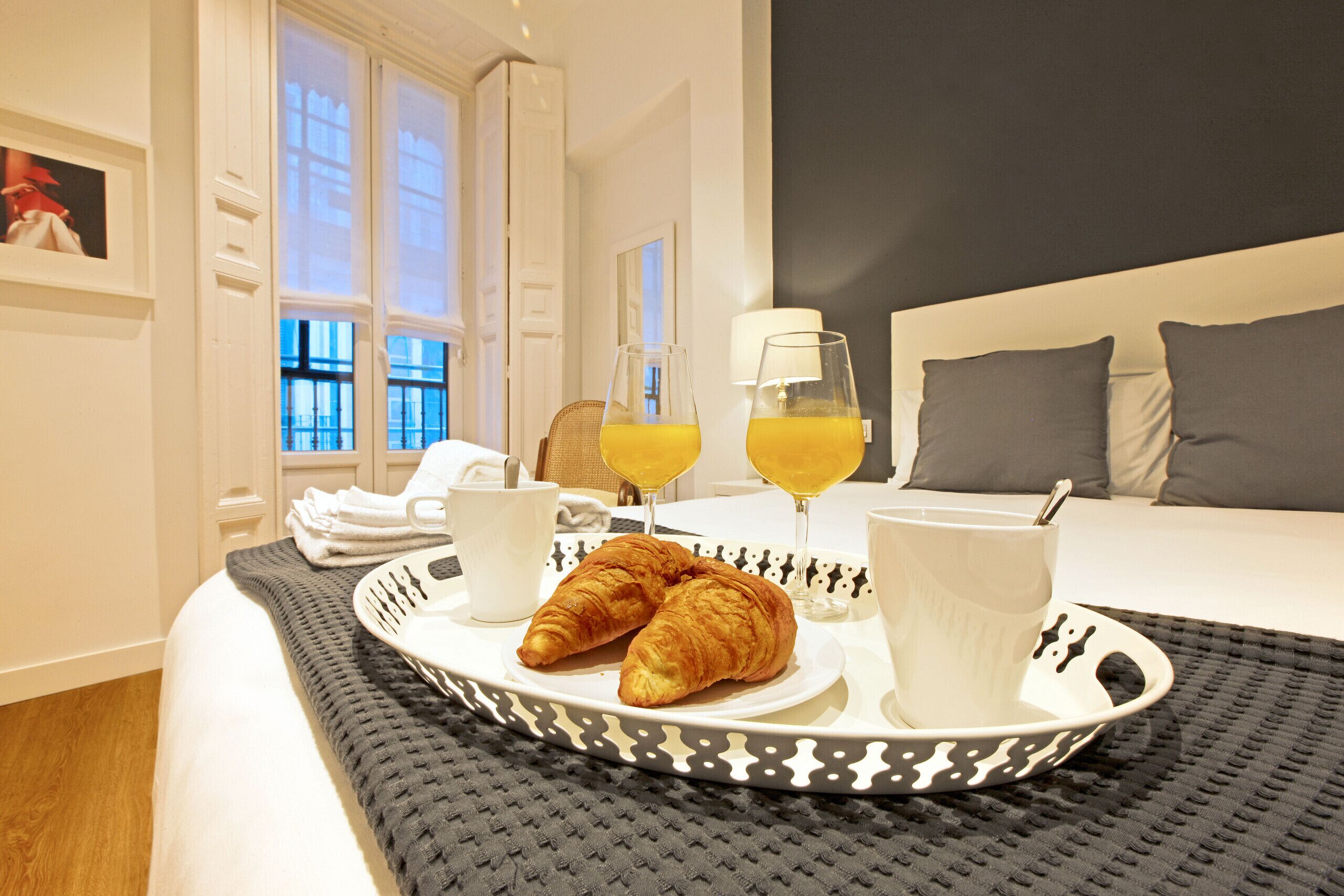 A neatly made breakfast tray with croissants, orange juice, and coffee on a bed in a hotel room.