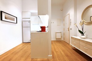 A modern kitchen with white appliances, a wooden floor, and a white cabinet with drawers. - Chueca Exclusive (Madrid)