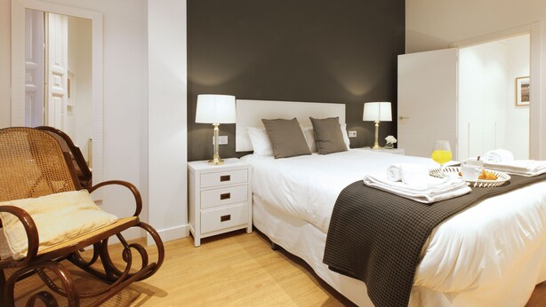 Habitación de hotel con cama, dos mesitas de noche con lámparas, una mecedora de madera y una bandeja de desayuno sobre la cama.