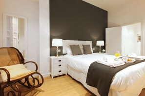 Ein Hotelzimmer mit einem Bett, zwei Nachttischen mit Lampen, einem hölzernen Schaukelstuhl und einem Frühstücksbrett auf dem Bett.