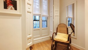 Una habitación con piso de madera, paredes blancas, una silla de mimbre con cojín y un cuadro en la pared.
