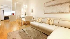 Una sala de estar moderna con una mesa de centro de vidrio, un sofá beige y una zona de comedor con sillas blancas.