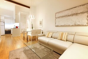 A modern living room with a glass coffee table, a beige sofa, and a dining area with white chairs.