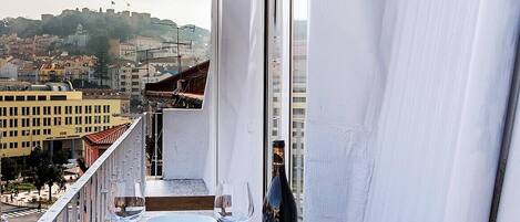 A balcony with a table set for two, overlooking a cityscape with buildings and a hill in the background.