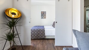 A bedroom with a bed, a bedside table, a floor lamp, and a door leading to another room. - Amazing Downtown Apt with balcony and fantastic view (Lisboa)