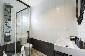 Een moderne badkamer met een douchecabine van glas, een witte wastafel en een toilet.