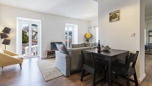 A modern living room with a sofa, dining table, and chairs. There is a TV and a plant on the table. - Amazing Downtown Apt with balcony and fantastic view (Lisboa)