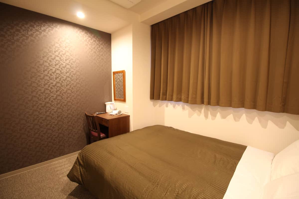 Ein Hotelzimmer mit einem großen Bett, einem kleinen Schreibtisch mit Stuhl und einem Fenster mit Vorhängen.