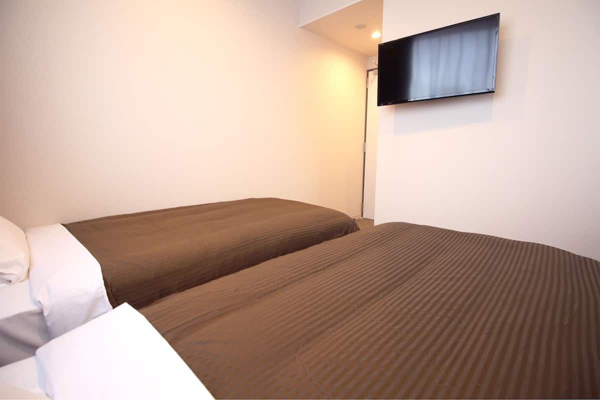 Ein Hotelzimmer mit zwei Betten, einem an der Wand montierten Flachbildfernseher und einem Nachttisch mit Lampe.
