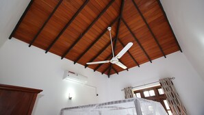 Una habitación con techo de madera inclinado, ventilador de techo, equipo de aire acondicionado y ventana con cortinas.
