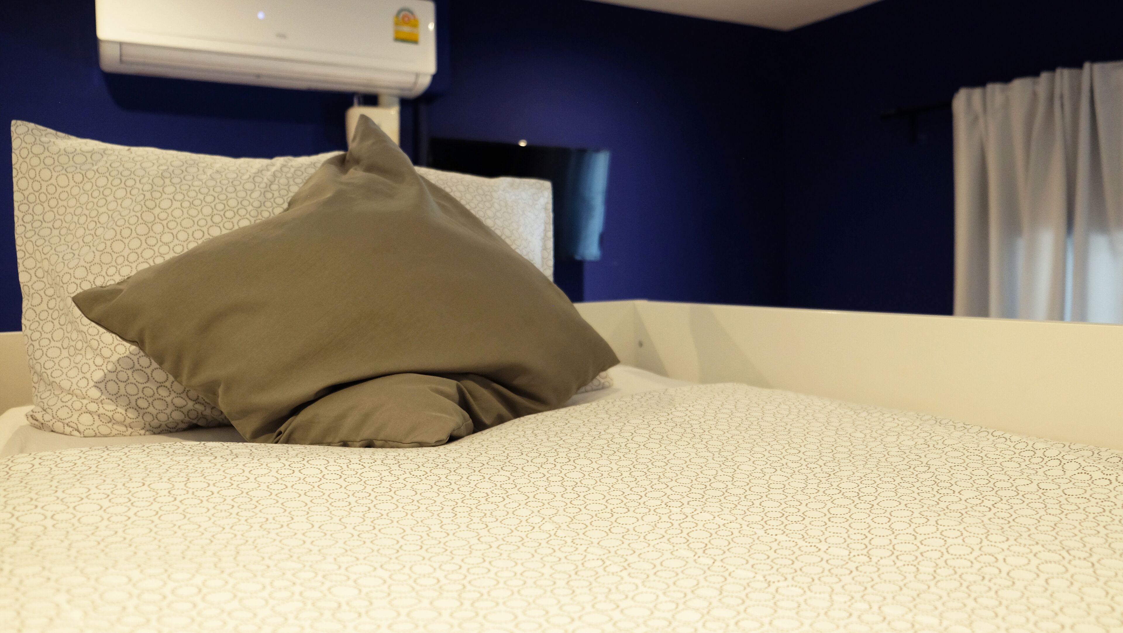 Une chambre d’hôtel avec un lit, un oreiller, un climatiseur fixé au mur et une fenêtre avec des rideaux.