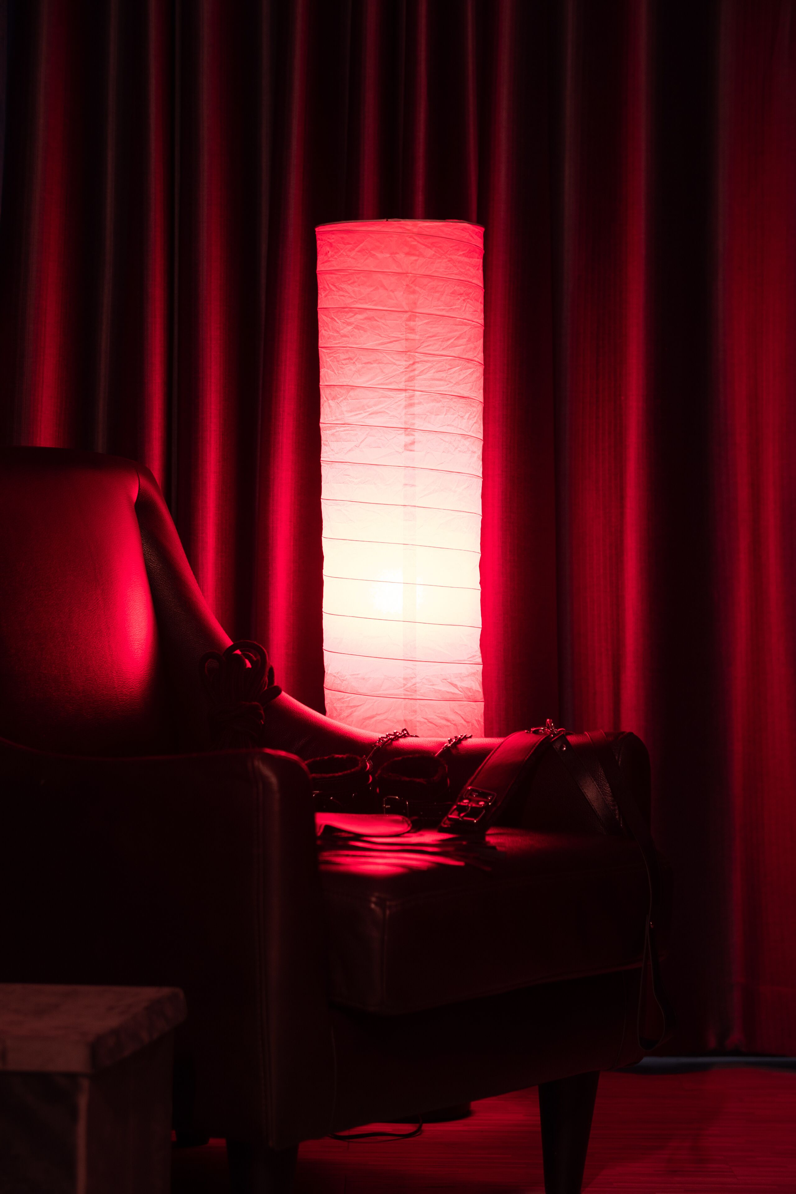 A room with a red-lit lamp, a leather chair, and a table with a remote control.