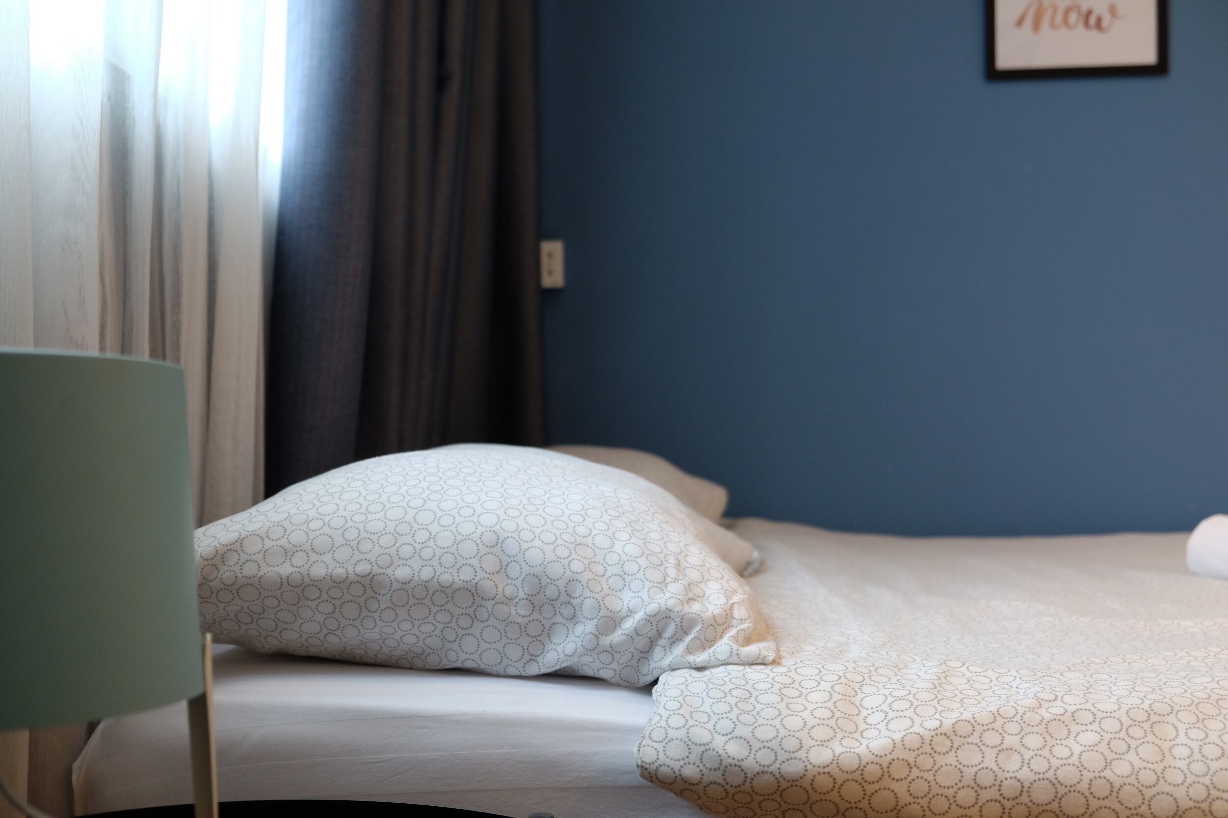 Una cama bien tendida con ropa de cama estampada, una pared azul y una palabra enmarcada en la pared.