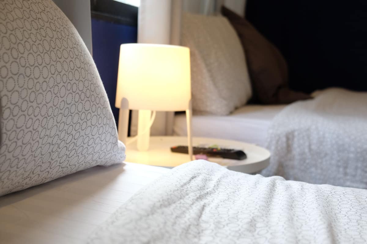 Habitació d'hotel amb dos llits, una taula de nit amb una làmpada i un comandament a la taula.