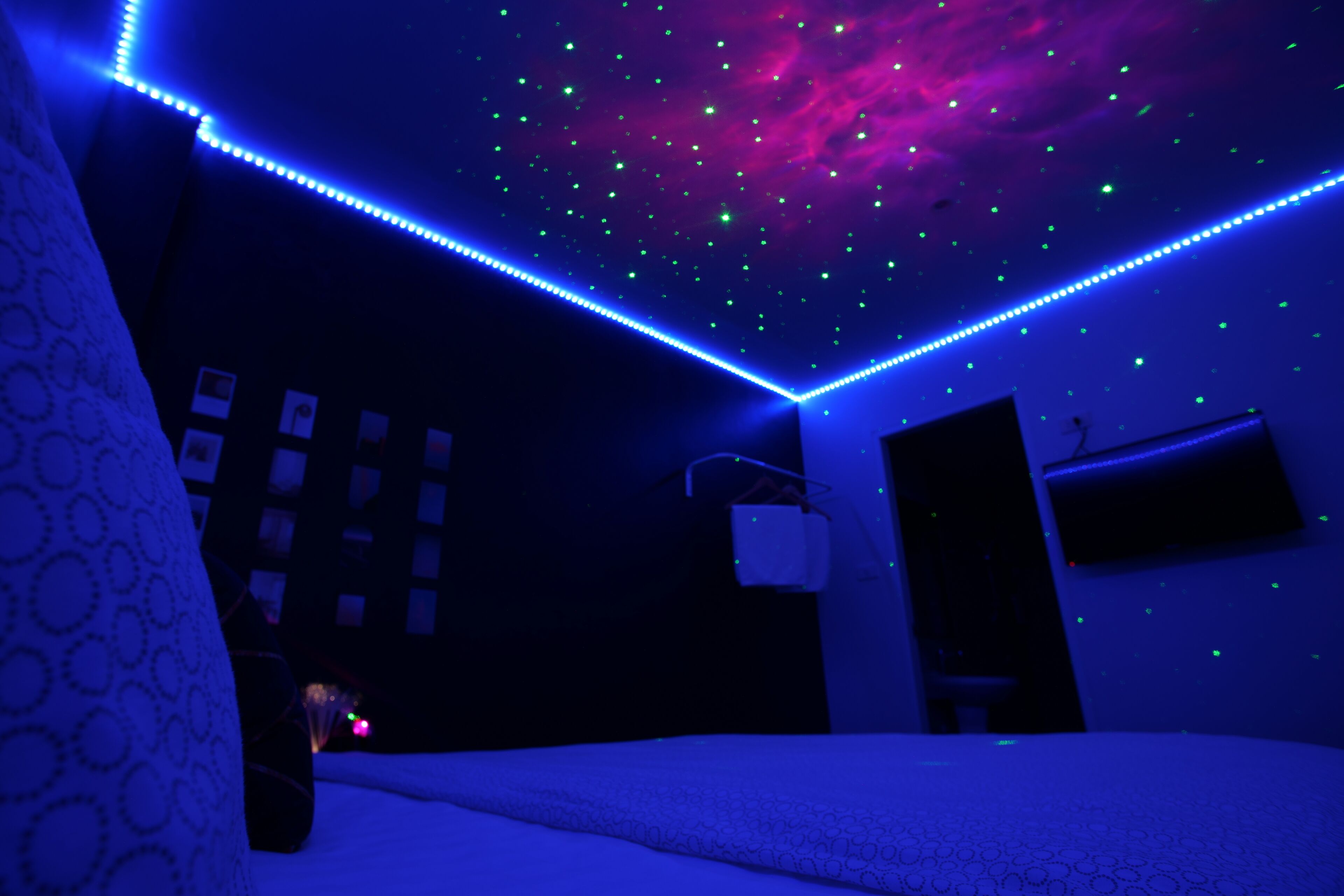 A room with a bed, a wall-mounted TV, and a ceiling with LED lights.