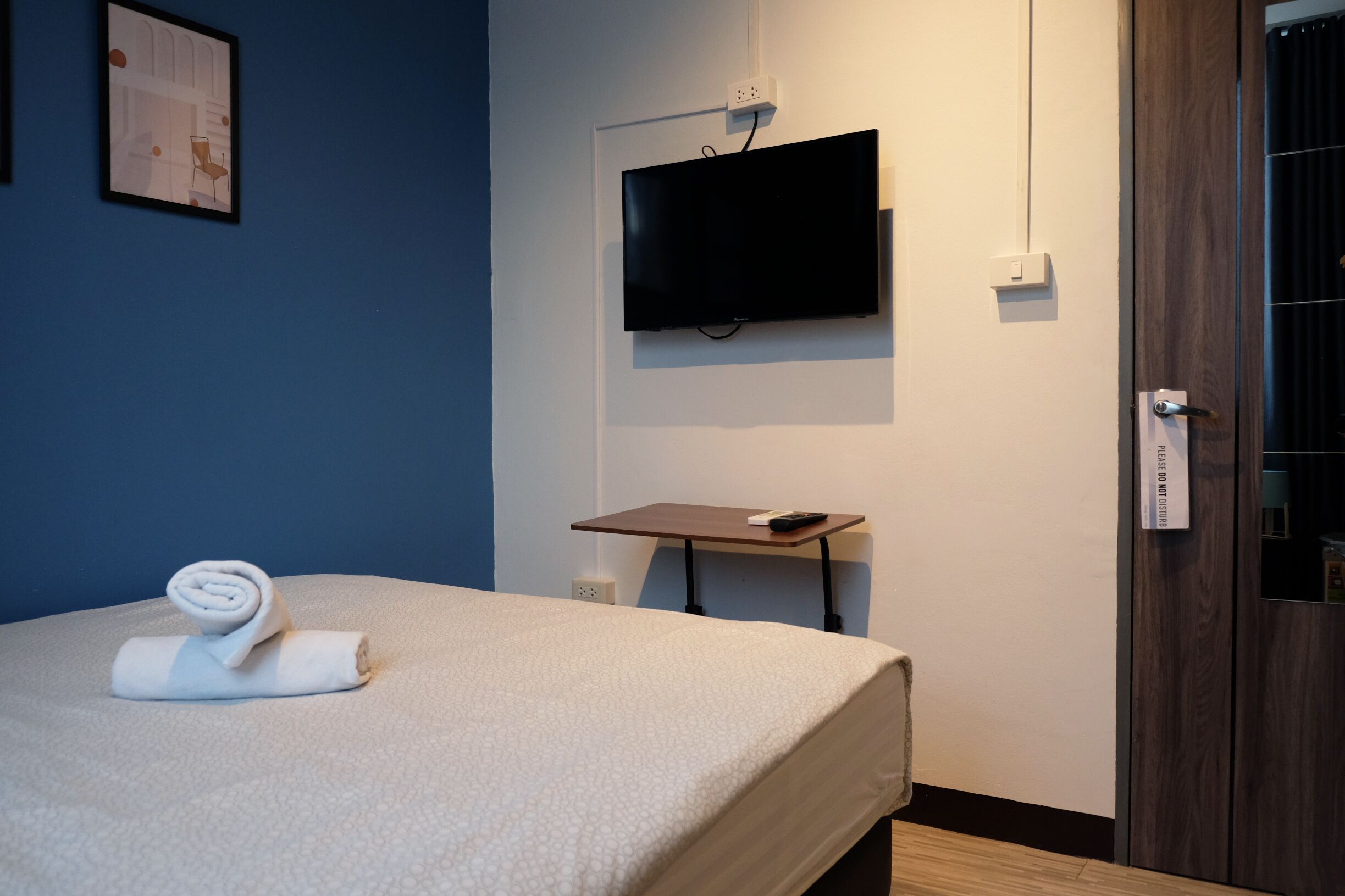 A hotel room with a bed, a TV mounted on the wall, a small table, and a door with a lock.