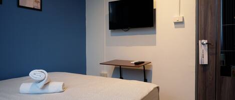 A hotel room with a bed, a TV mounted on the wall, a small table, and a door with a lock.