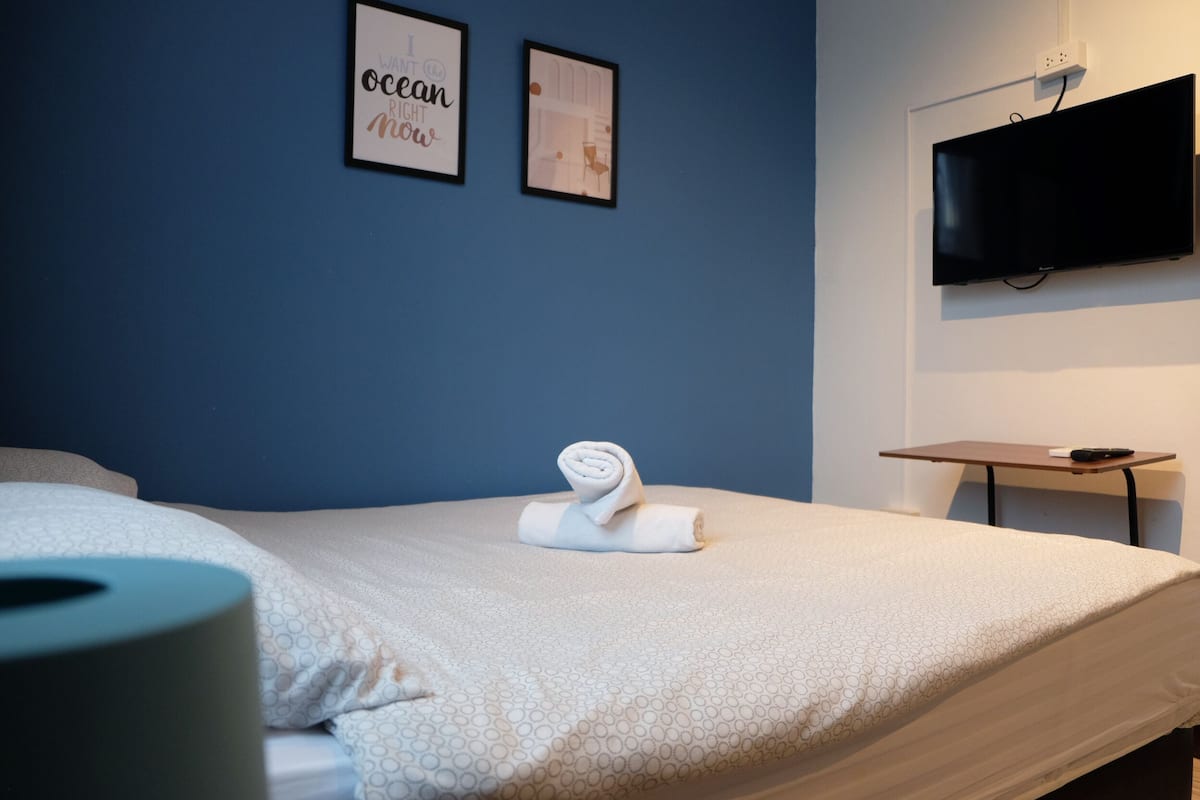 Una habitació d'hotel amb un llit, una televisió penjada a la paret i dos quadres emmarcados a la paret.