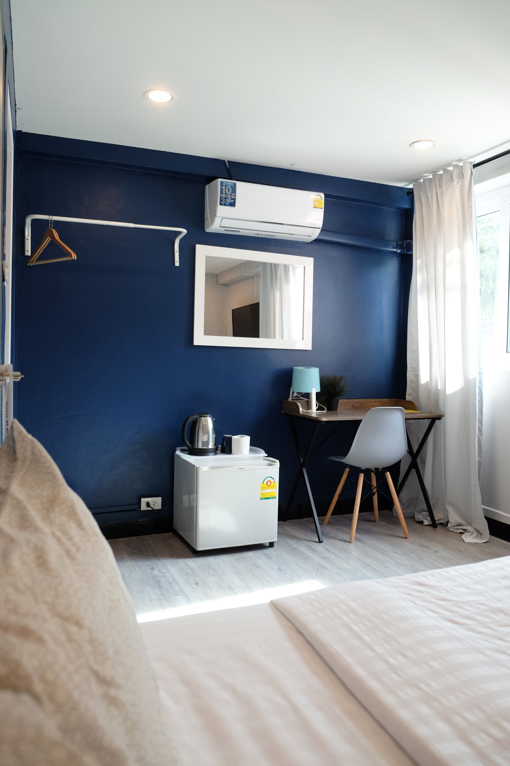 A room with a bed, a desk, a chair, a mirror, an air conditioner, and a window with curtains.