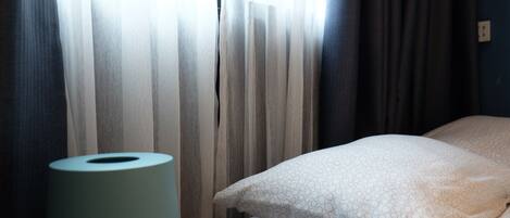 Una habitación de hotel con una cama, un almohadón, un rollo de papel higiénico y una ventana con cortinas.