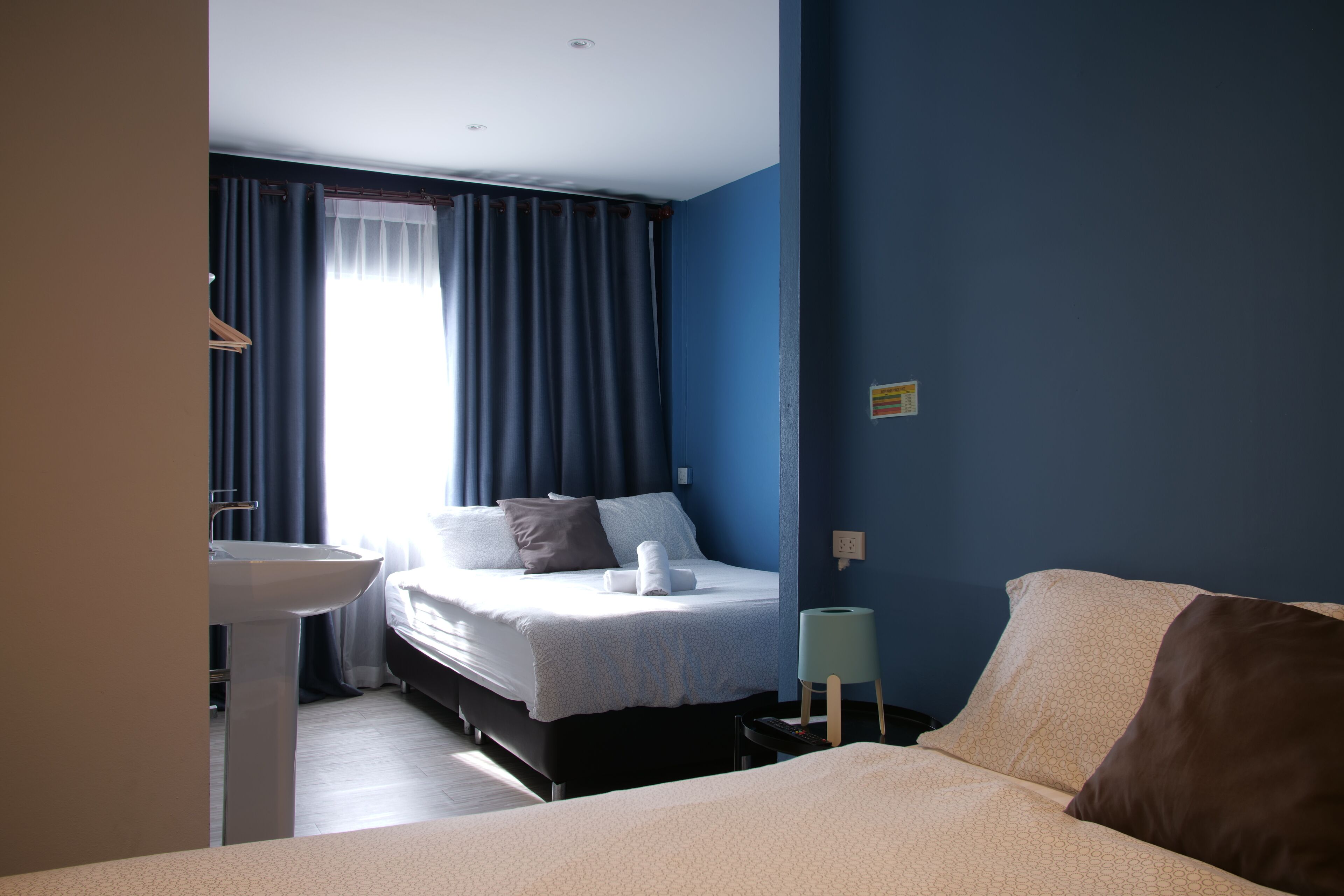Una habitación de hotel con cama, mesita de noche y ventana con cortinas.