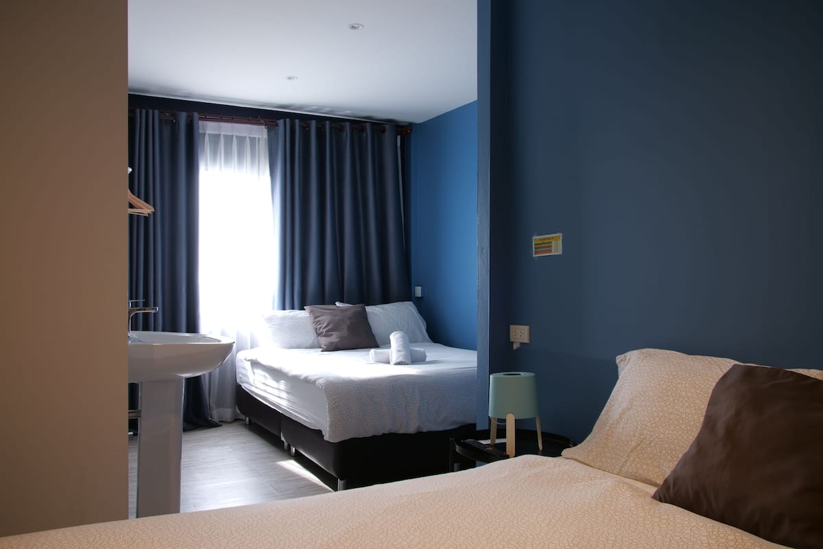 Una habitació d'hotel amb llit, taula de nit i finestra amb cortines.